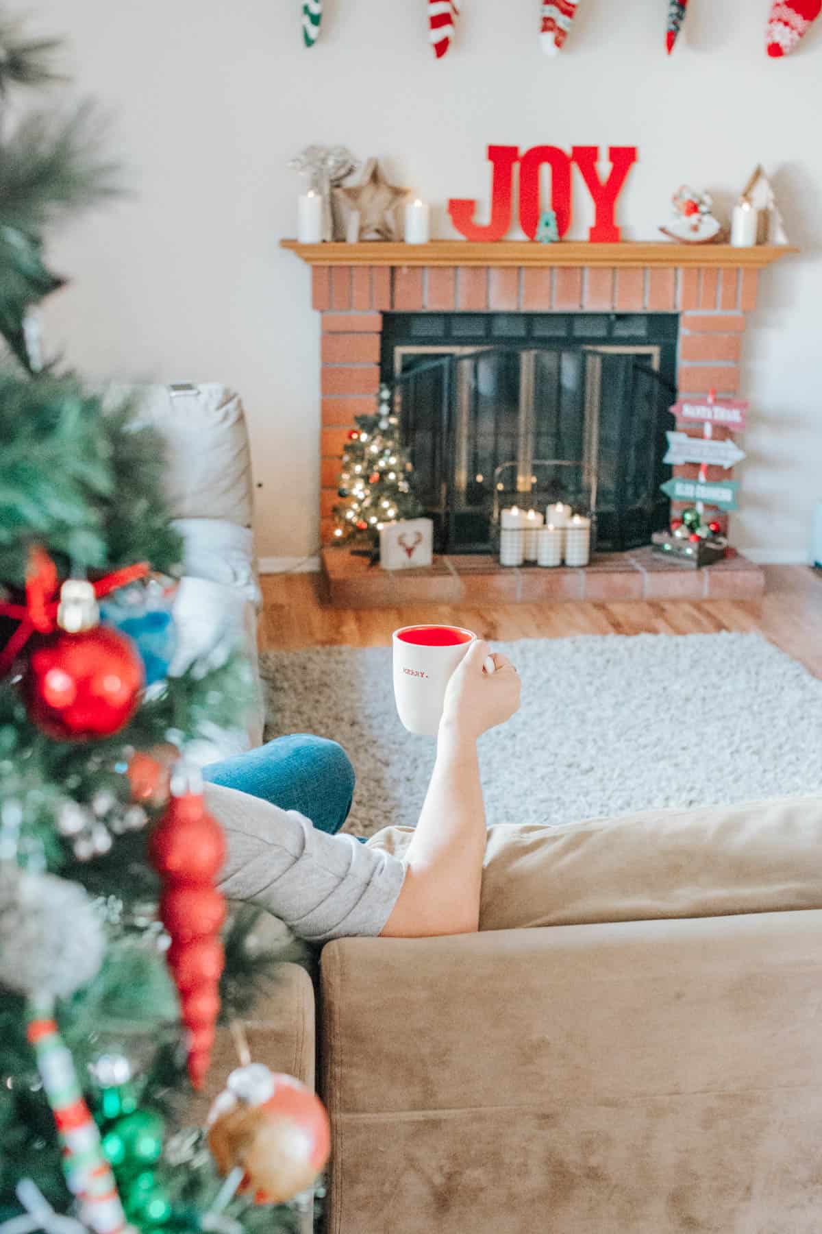 A woman's arm holding a mug with her fireplace in the background.