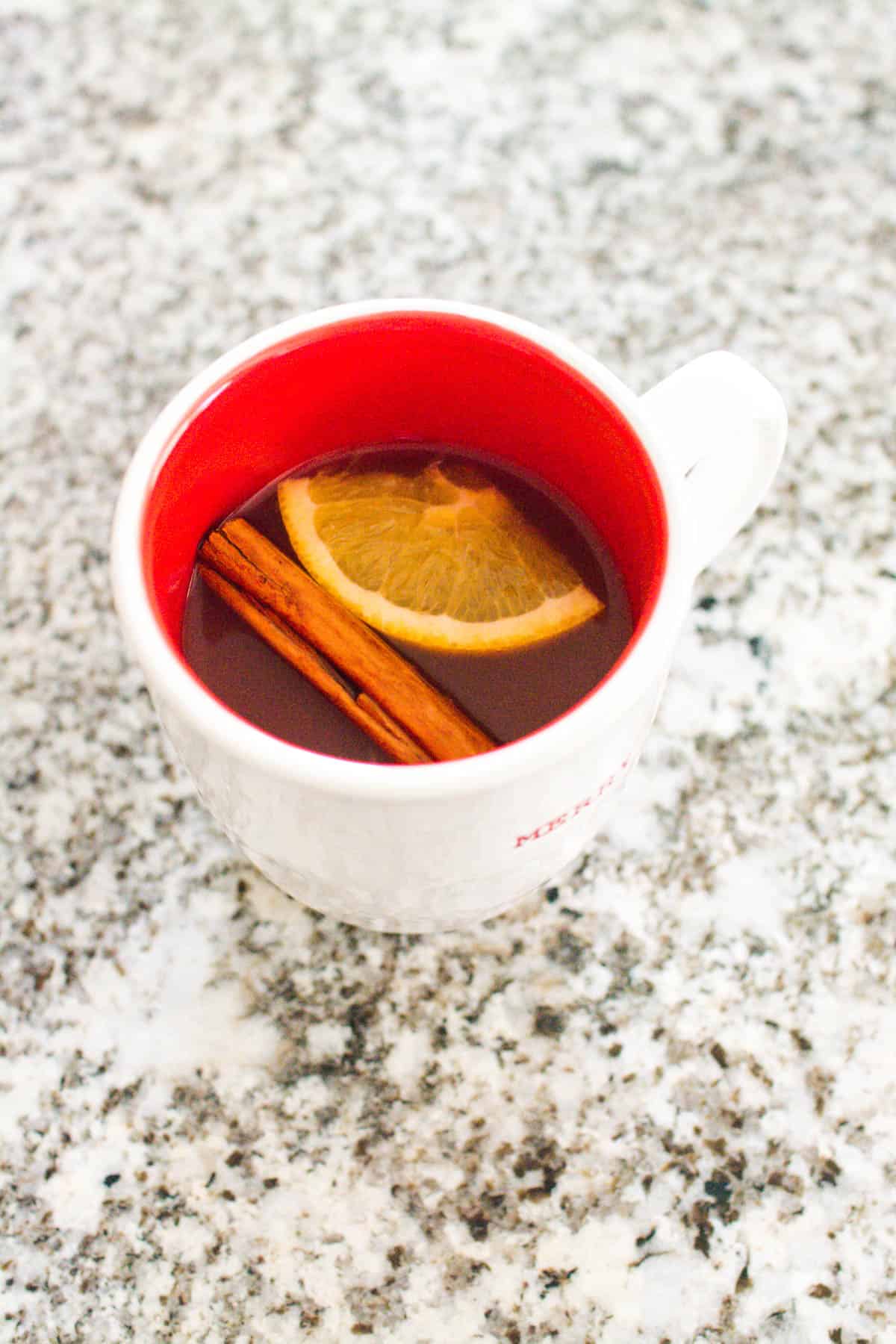 Overhead view of a mug holding warm Cranberry Punch with an orange wheel and cinnamon stick for garnish. 