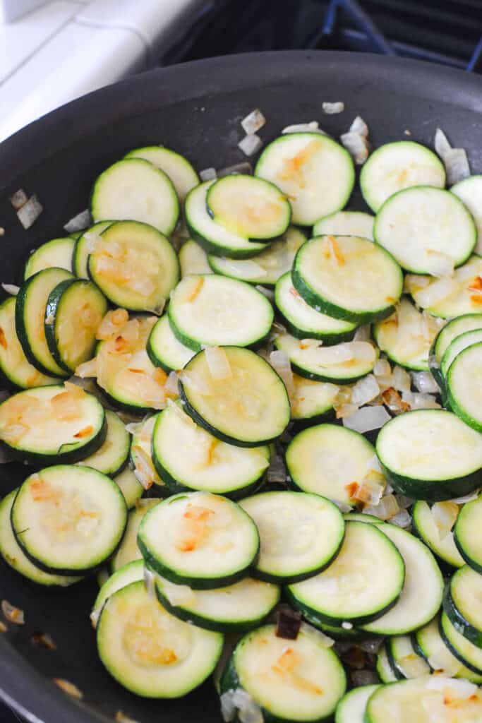 Zucchini and onions being sauteed in a pan.