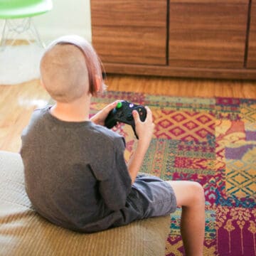 Square image of a boy holding an Xbox gaming controller while playing Fortnite.