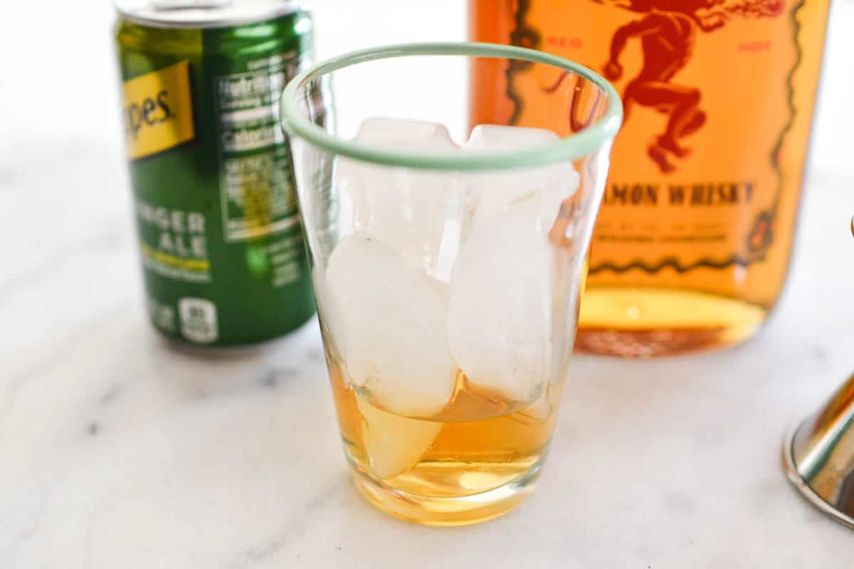 Close up of a small cocktail glass filled with ice and a little Fireball whiskey.