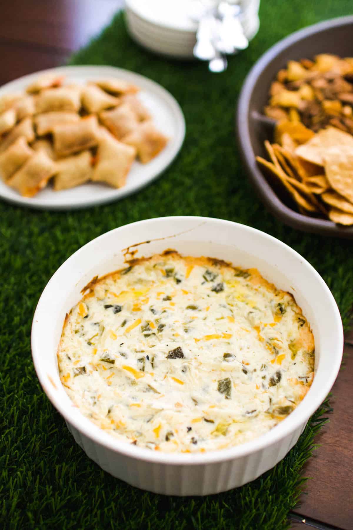 Close up of a warm green chile dip in a baking dish next to other snacks.