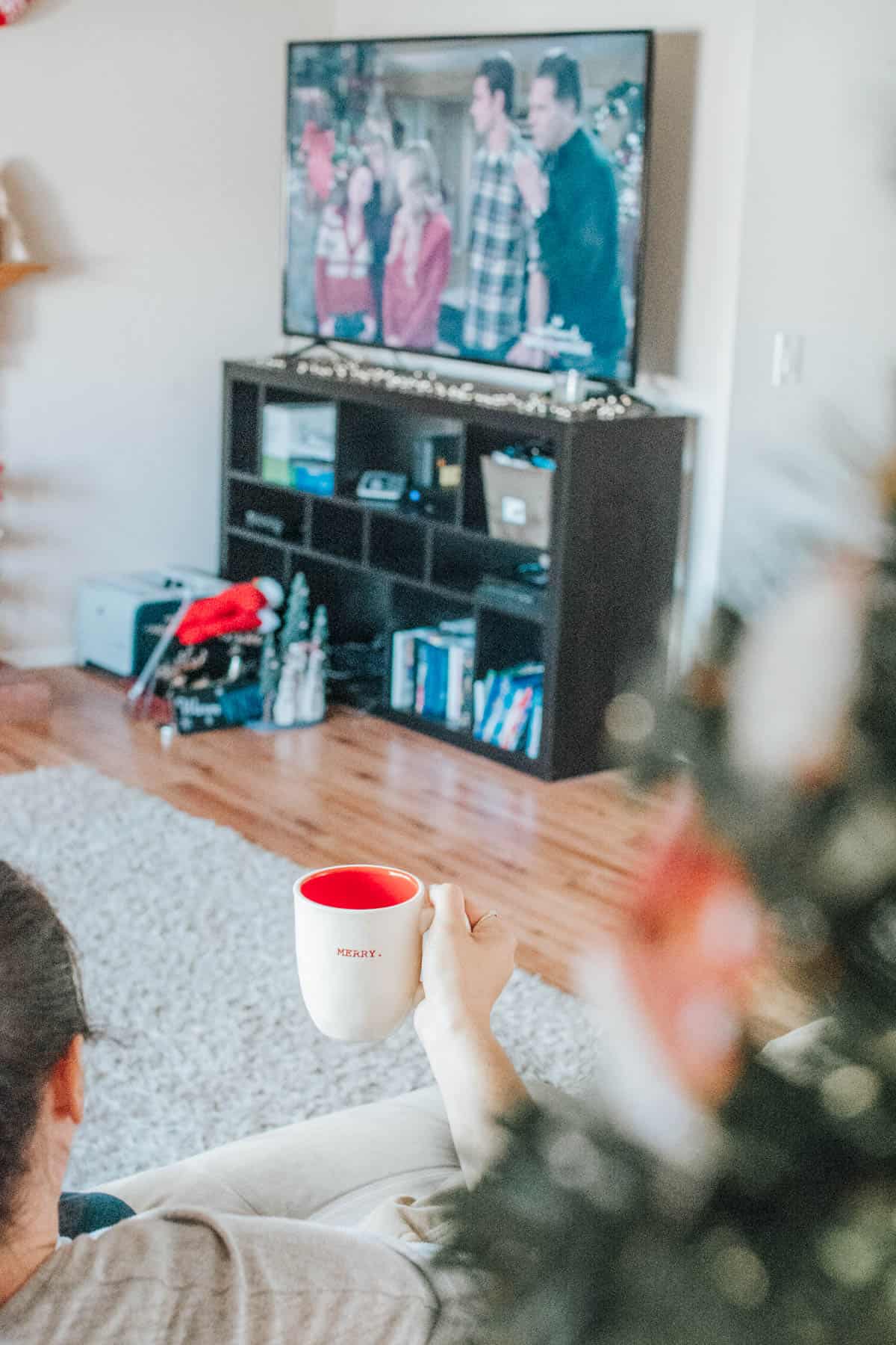 Woman holding coffee mug on a couch while watching TV.