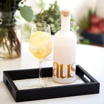Cocktail in a wine glass on a small tray on a table.