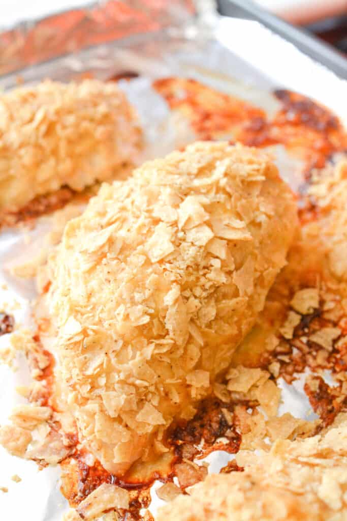 Close up of baked chicken breasts coated in crushed tortilla chips.