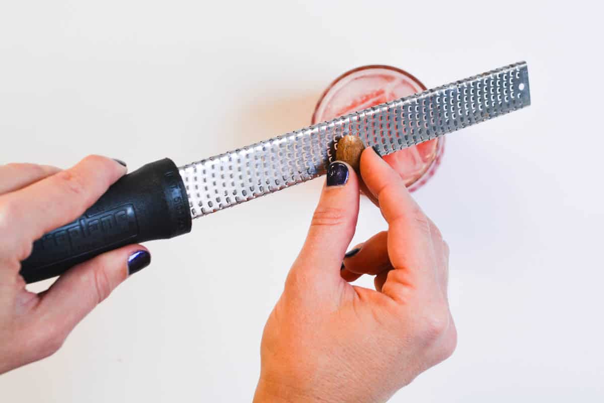 Woman grating fresh nutmeg over the top of a cocktail.