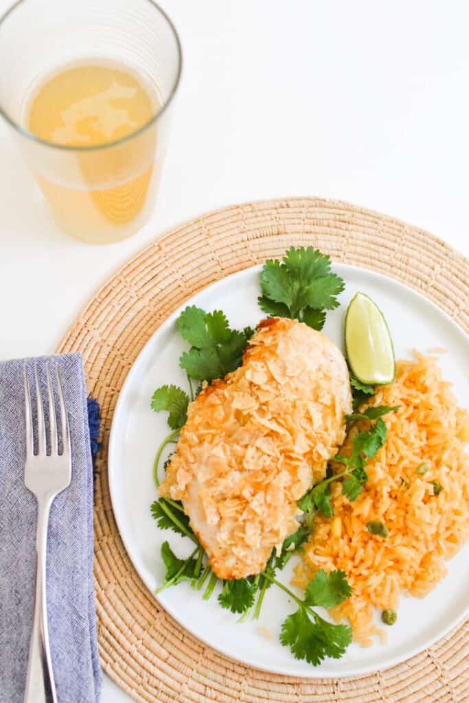 Tortilla chip crusted chicken breast on a plate next to rice.