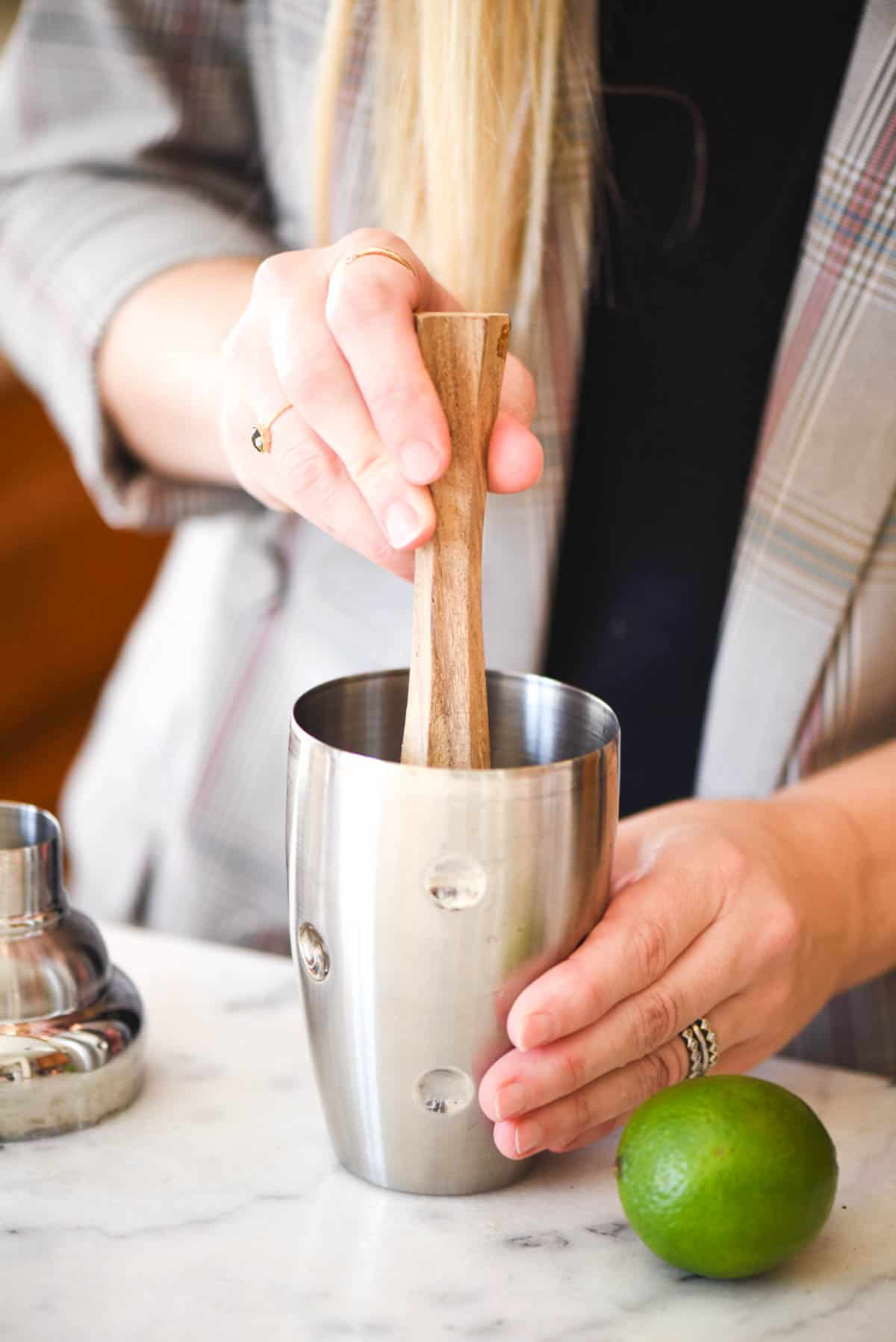 Woman muddling a cocktail in a cocktail shaker.