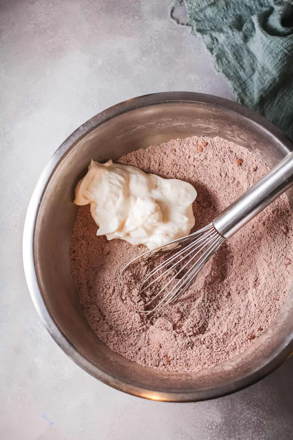 Dry ingredients with cocoa in a bowl with a glob of mayonnaise on top and whisk.