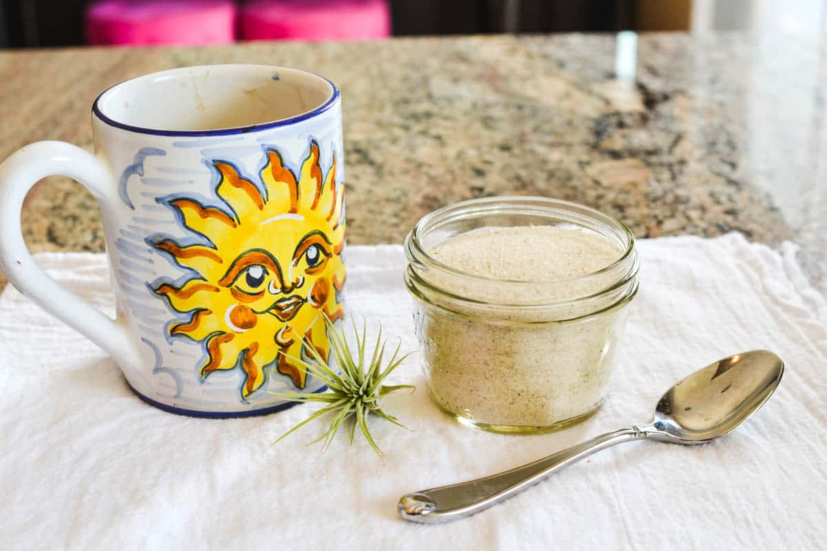 Small bowl of sugar on a counter next to a coffee mug with a sun on it.