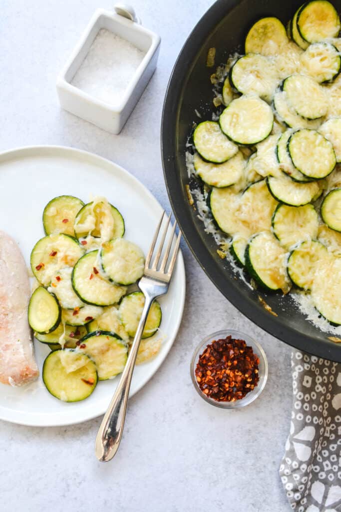 A close up of a dinner plate with a serving zucchini topped with parmesan.