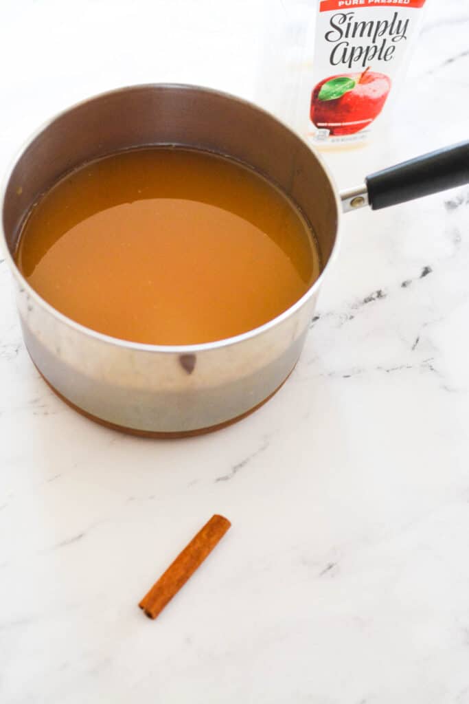 Saucepan on a counter with apple cider next to a cinnamon stick.
