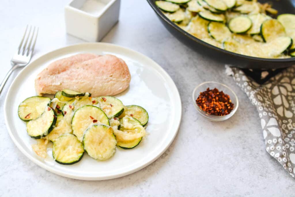 A dinner plate with chicken and zucchini on a table next to a pan.