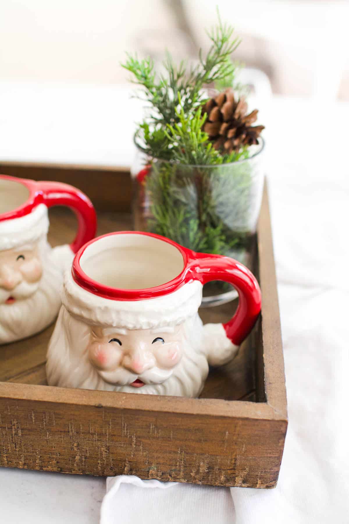 Tray on a table with two Santa Face mugs next to some holiday greenery.