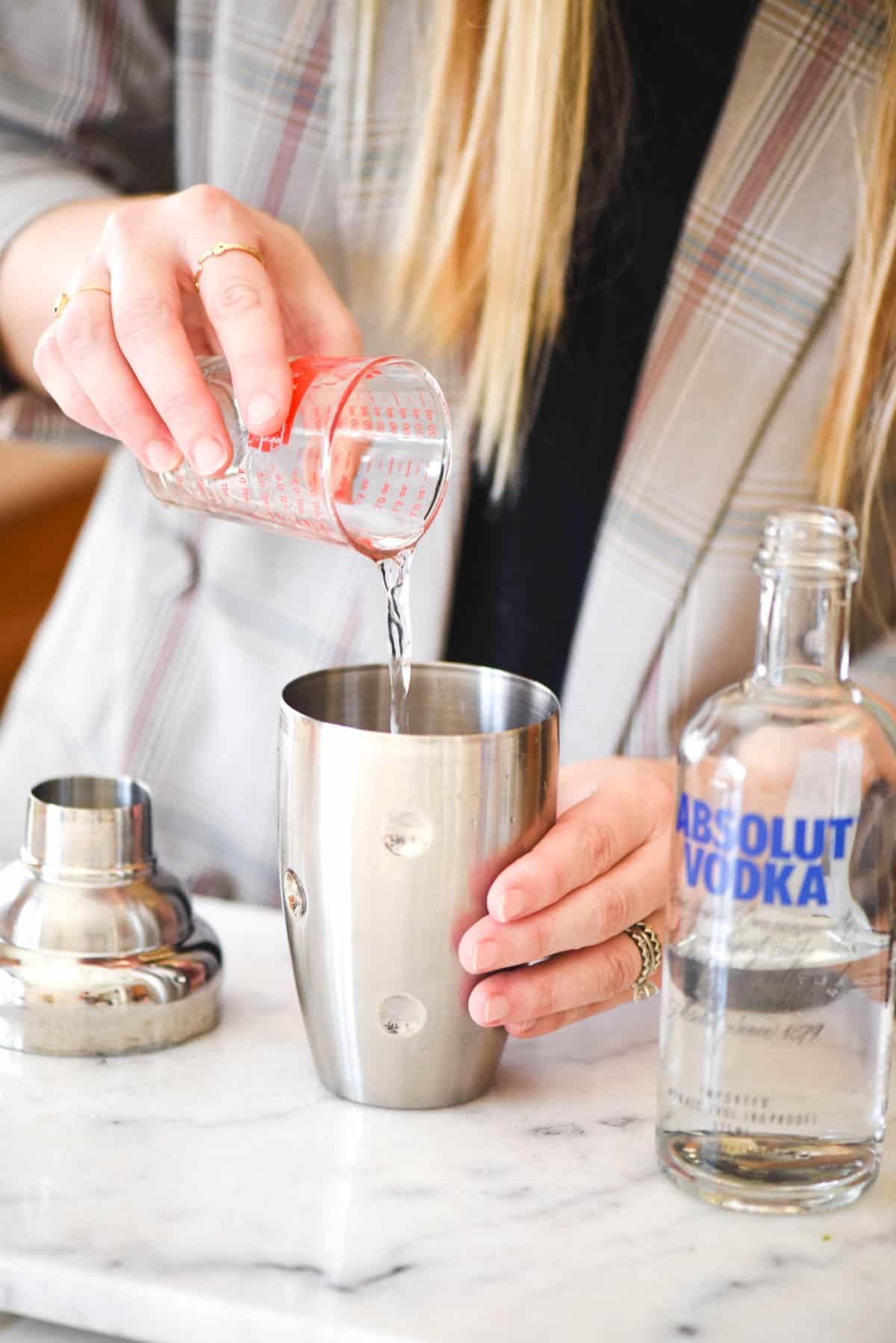 Woman adding tequila to a cocktail shaker.