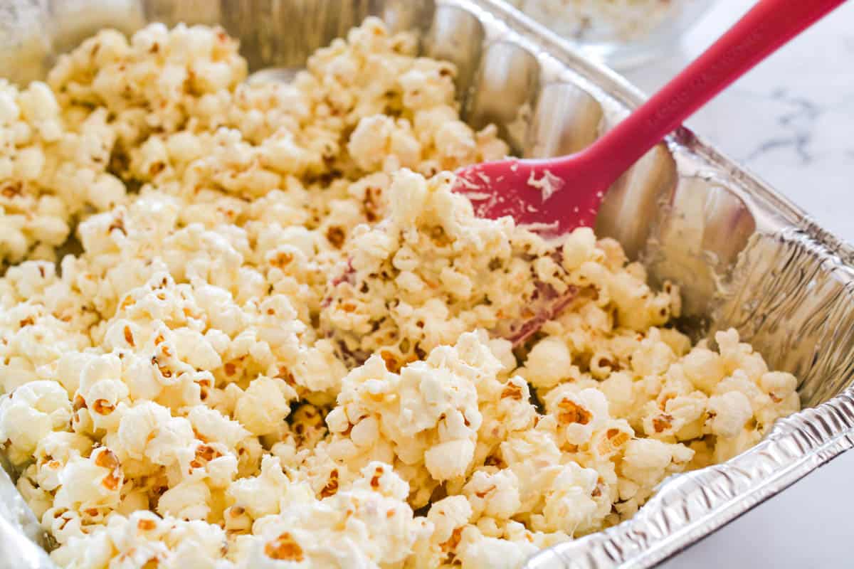 White chocolate being mixed into popcorn in a disposable pan.