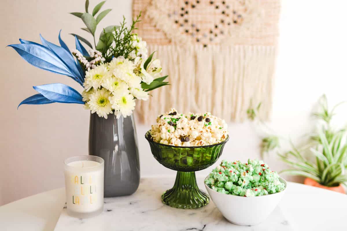 Two bowls of popcorn on a table next to a flower arrangement and candle.