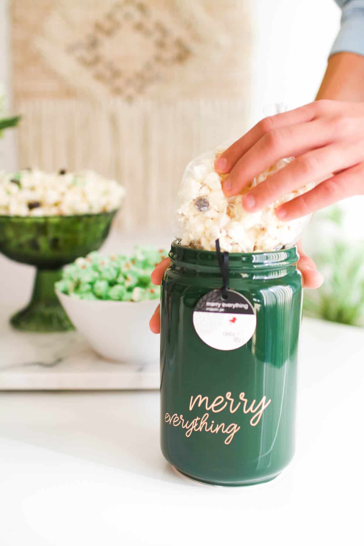 Adding a bag of white chocolate popcorn to a green holiday jar.
