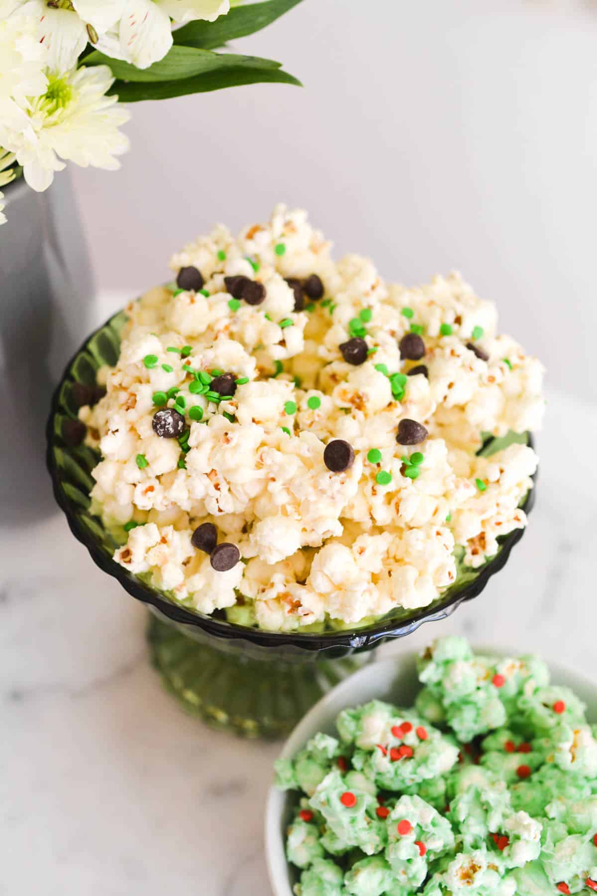 Close up of white chocolate popcorn with chocolate chips and green sprinkles.