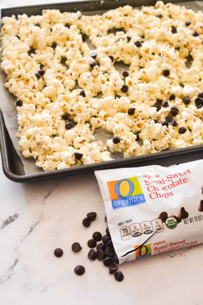 A tray of popcorn next to an open bag of chocolate chips with some spilling out on the counter.