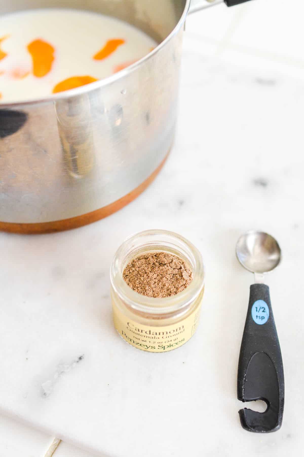 A saucepan on a counter next to a small jar of ground cardamom.