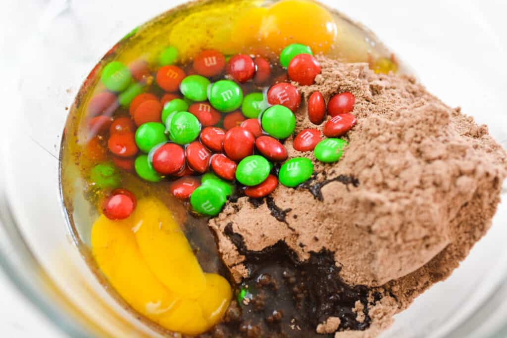 Close up of cookie ingredients in a mixing bowl with chocolate cake mix and M&Ms.