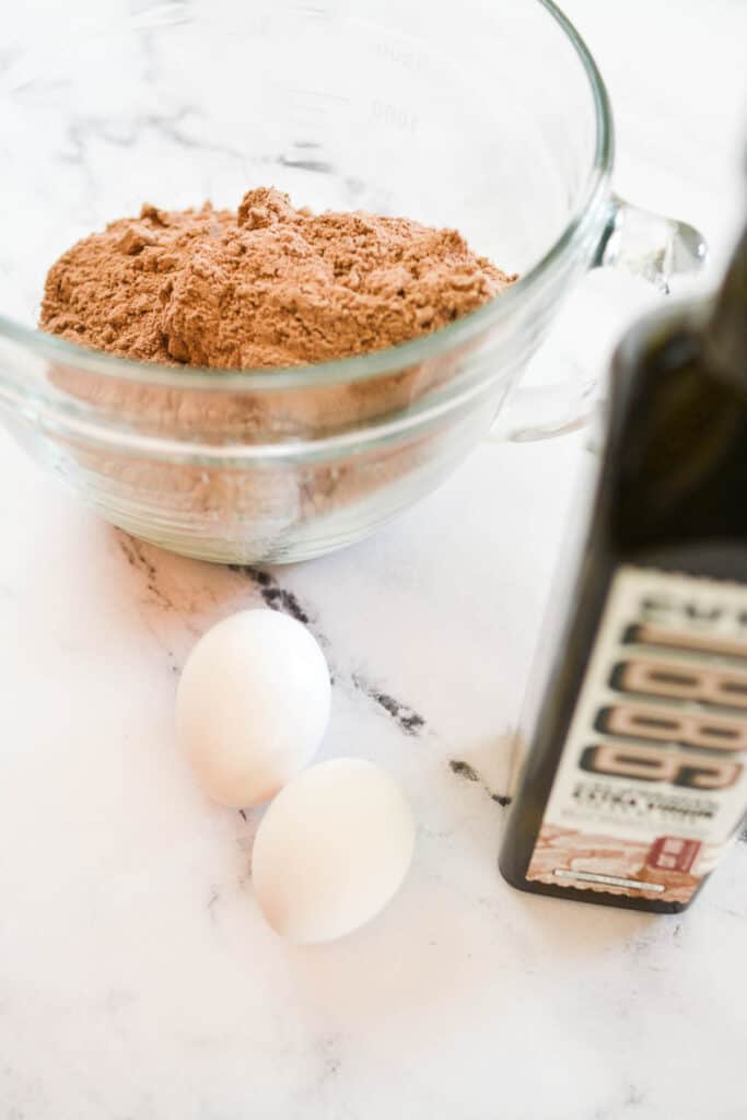 A mixing bowl with cake mix next to eggs and olive oil on a counter.