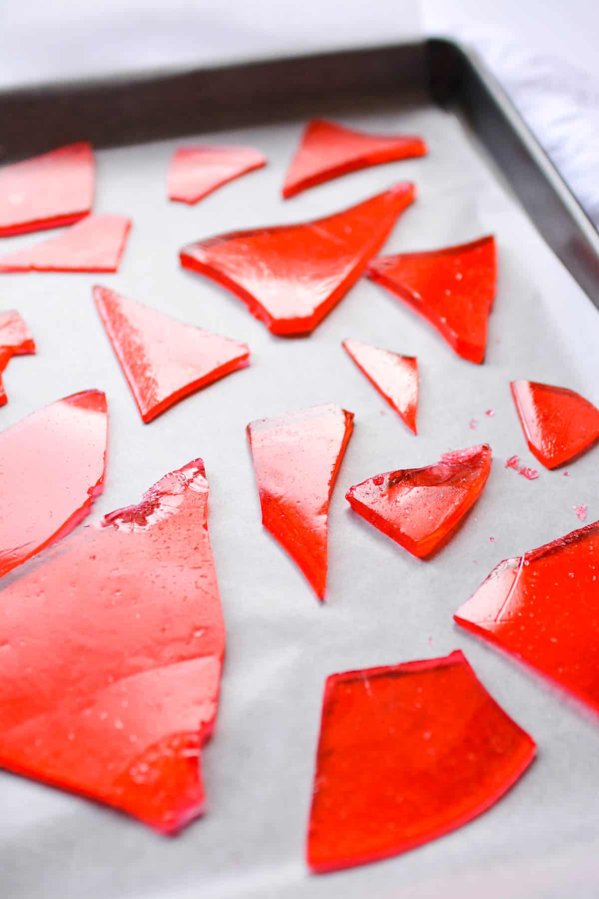 Close up of pieces of red cinnamon candy on a cookie sheet topped with waxed paper.