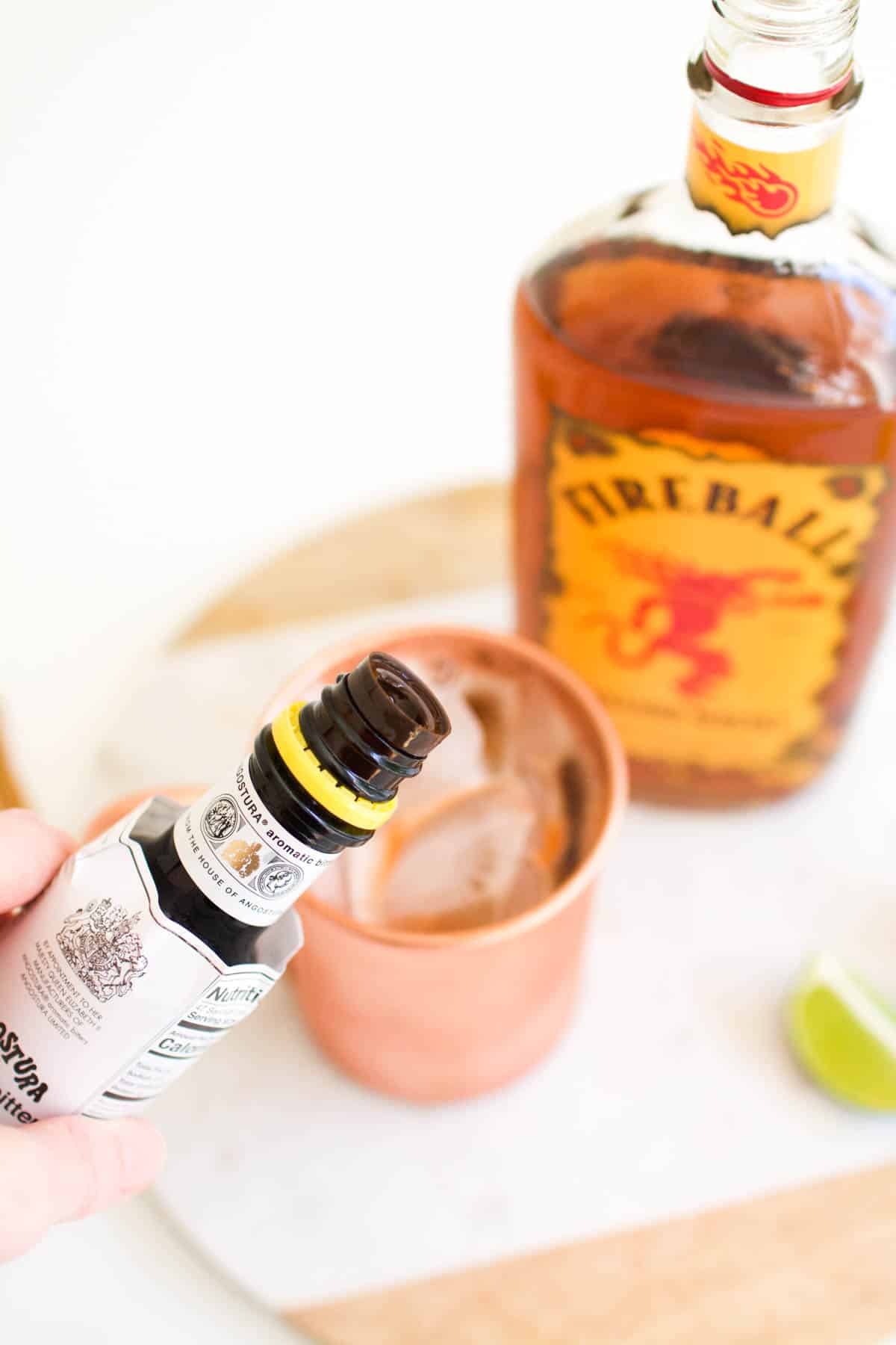 Woman holding a bottle of bitters over a copper moscow mule mug.