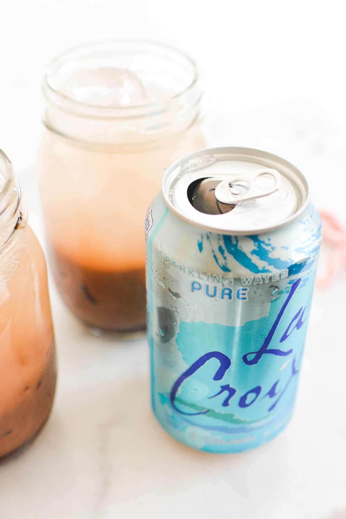 Close up of a can of club soda next to 2 jars holding a chocolate soda.