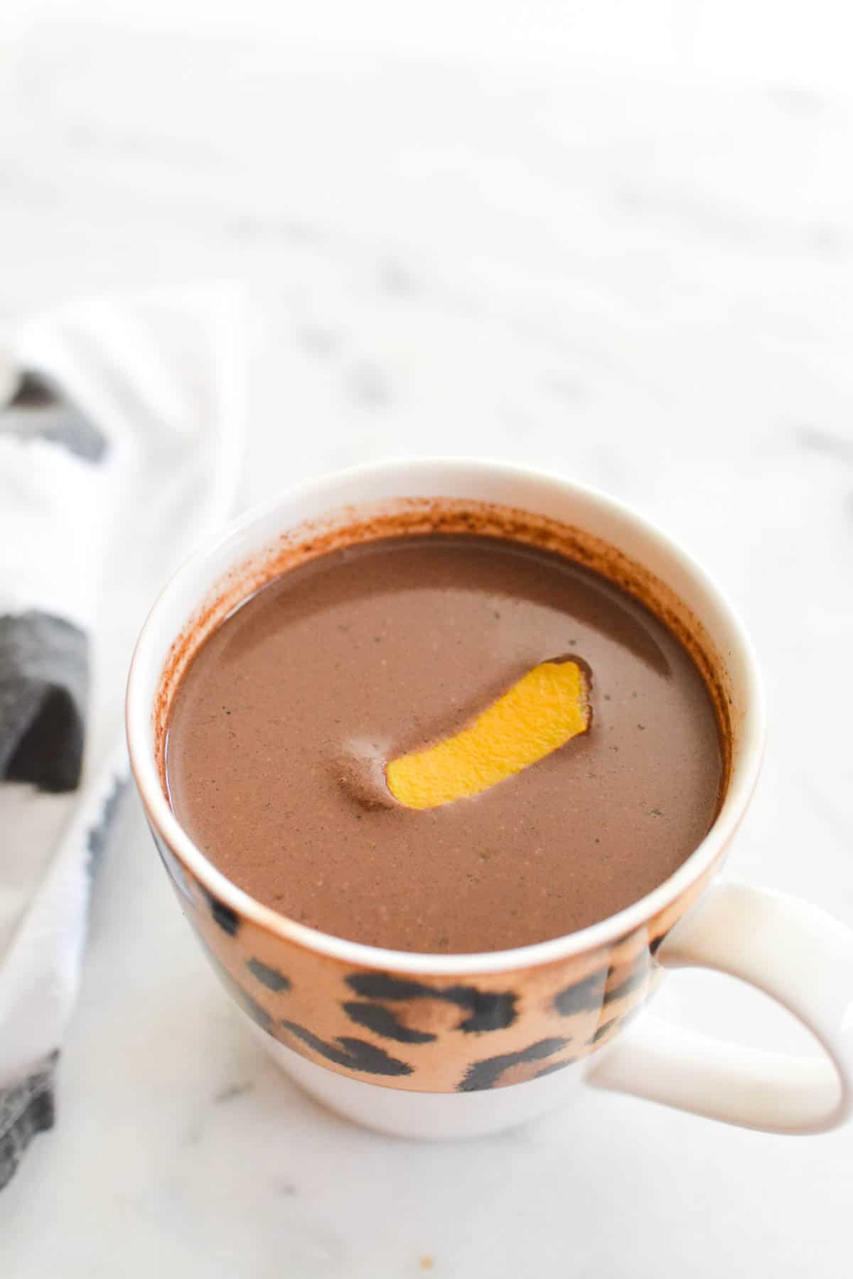 Mug of hot cocoa on a counter with a piece of orange peel on top.