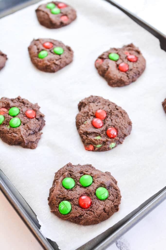 Baked chocolate cookies with holiday M&Ms on a baking sheet.