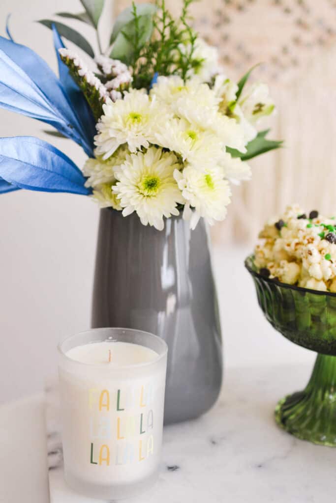 Close up of a holiday candle next to a vase of flowers.