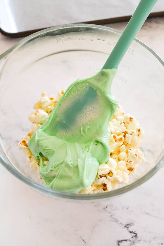 Green colored white chocolate on top of popped popcorn before mixing.