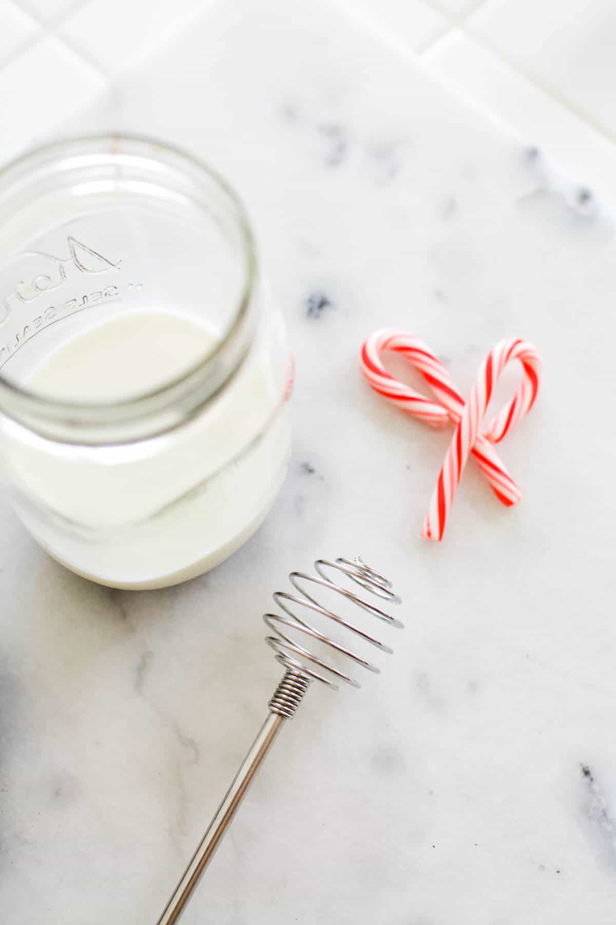 A jar of milk on the counter next to a small whisk and two mini candy canes.