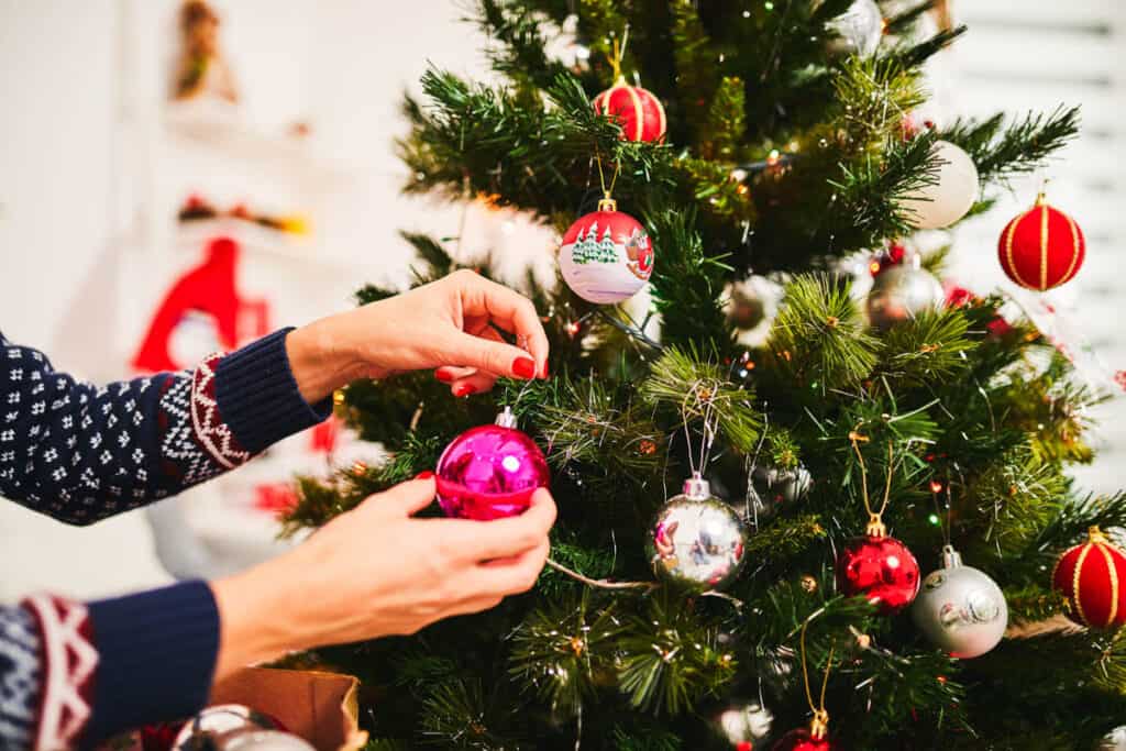 Woman putting an ornament on a Christmas tree.