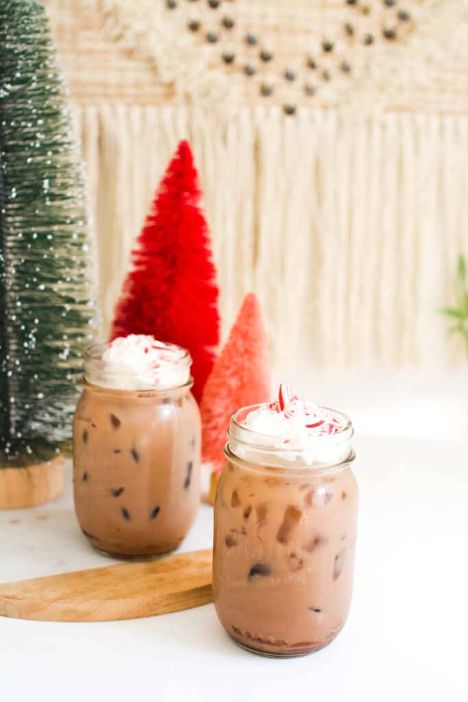 Jars of chocolate egg cream soda on a table next to bottle brush Christmas trees.