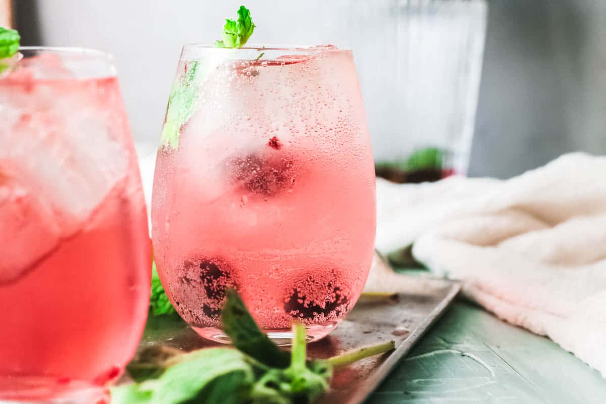 Close up of a pink cocktail with blackberries in it.