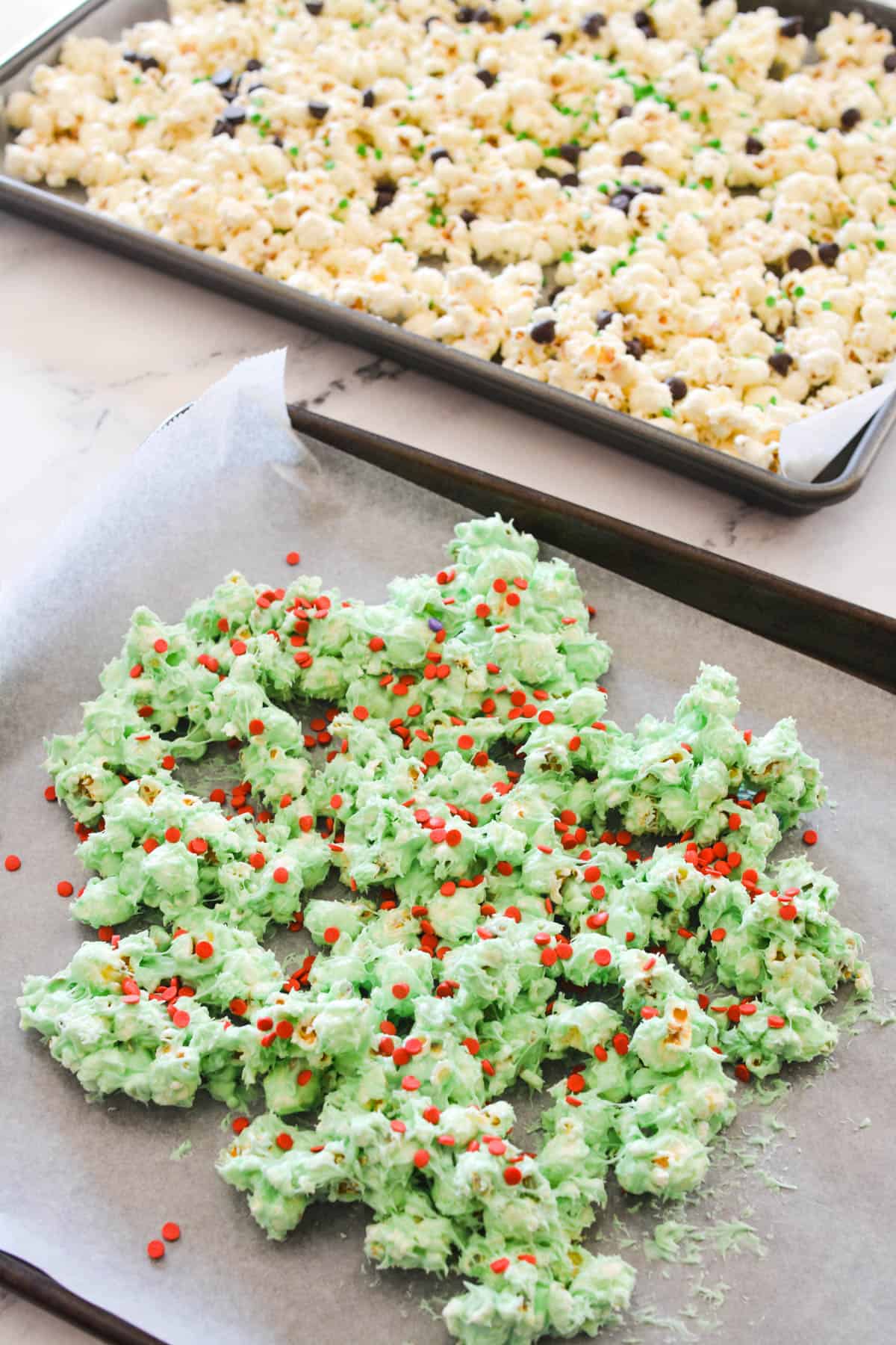Green colored white chocolate covered popcorn with sprinkles on a baking sheet.