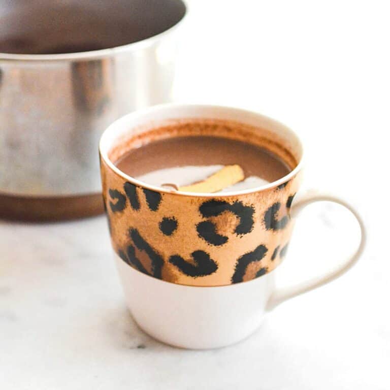 Leopard print mug filled with hot chocolate garnished with a piece of orange rind.
