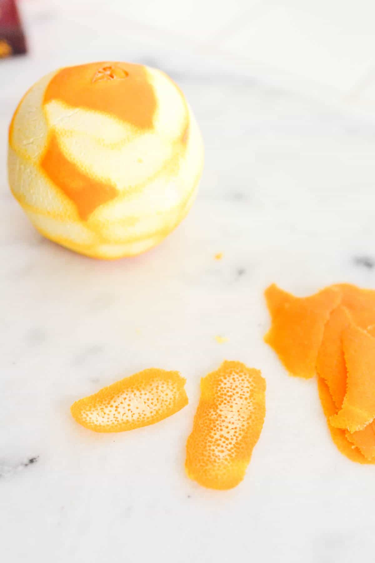 An orange with the peel peeled off and on the counter next to it.