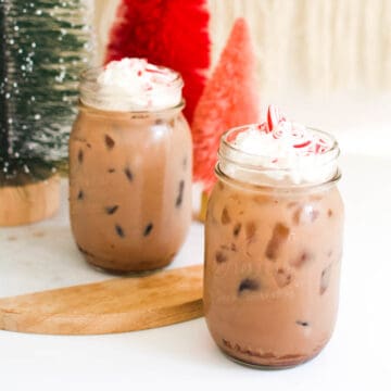 2 jars on a table with a chocolate drink topped with whipped cream and crushed candy cane.