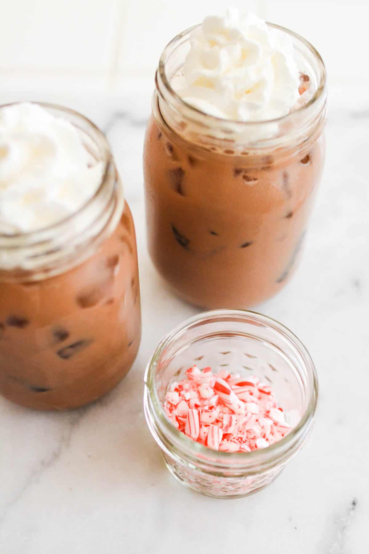 Two jars on a counter holding chocolate egg cream soda next to a small dish with crushed candy cane.