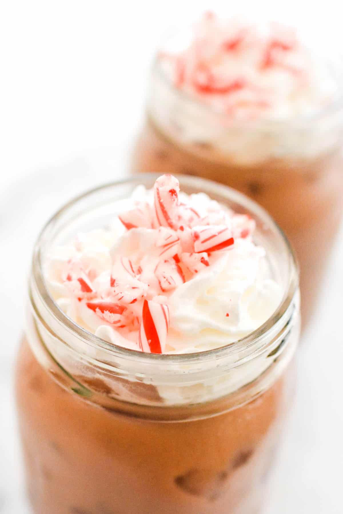 Close up of crushed candy cane on top of whipped cream on drinks in jars.