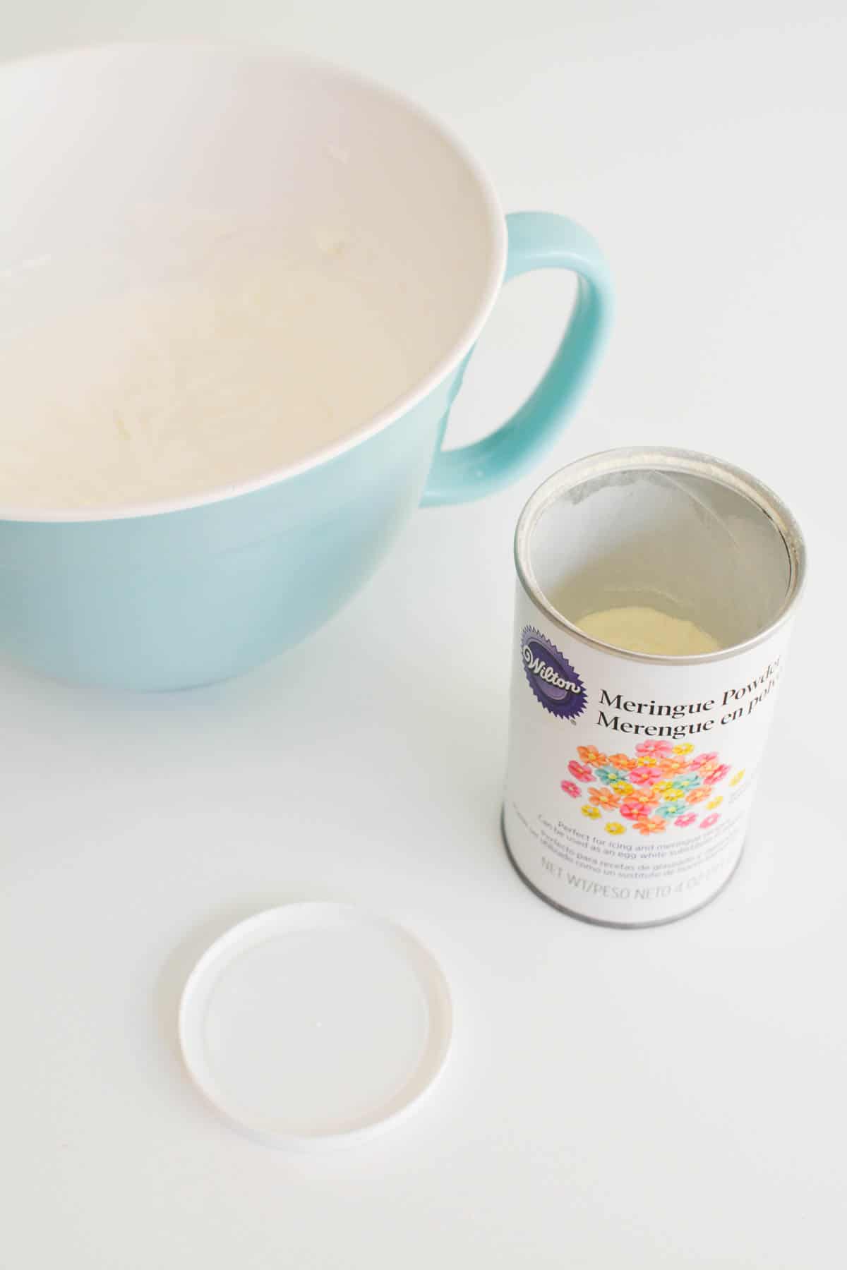 Can of meringue powder on a table next to a bowl.