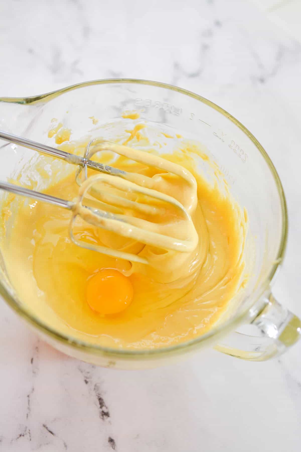 Mixing bowl with cake batter and an egg with a mixer in it.