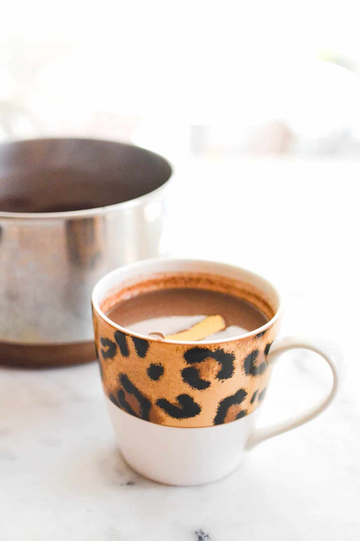 A mug with a leopard print on a counter next to a saucepan.