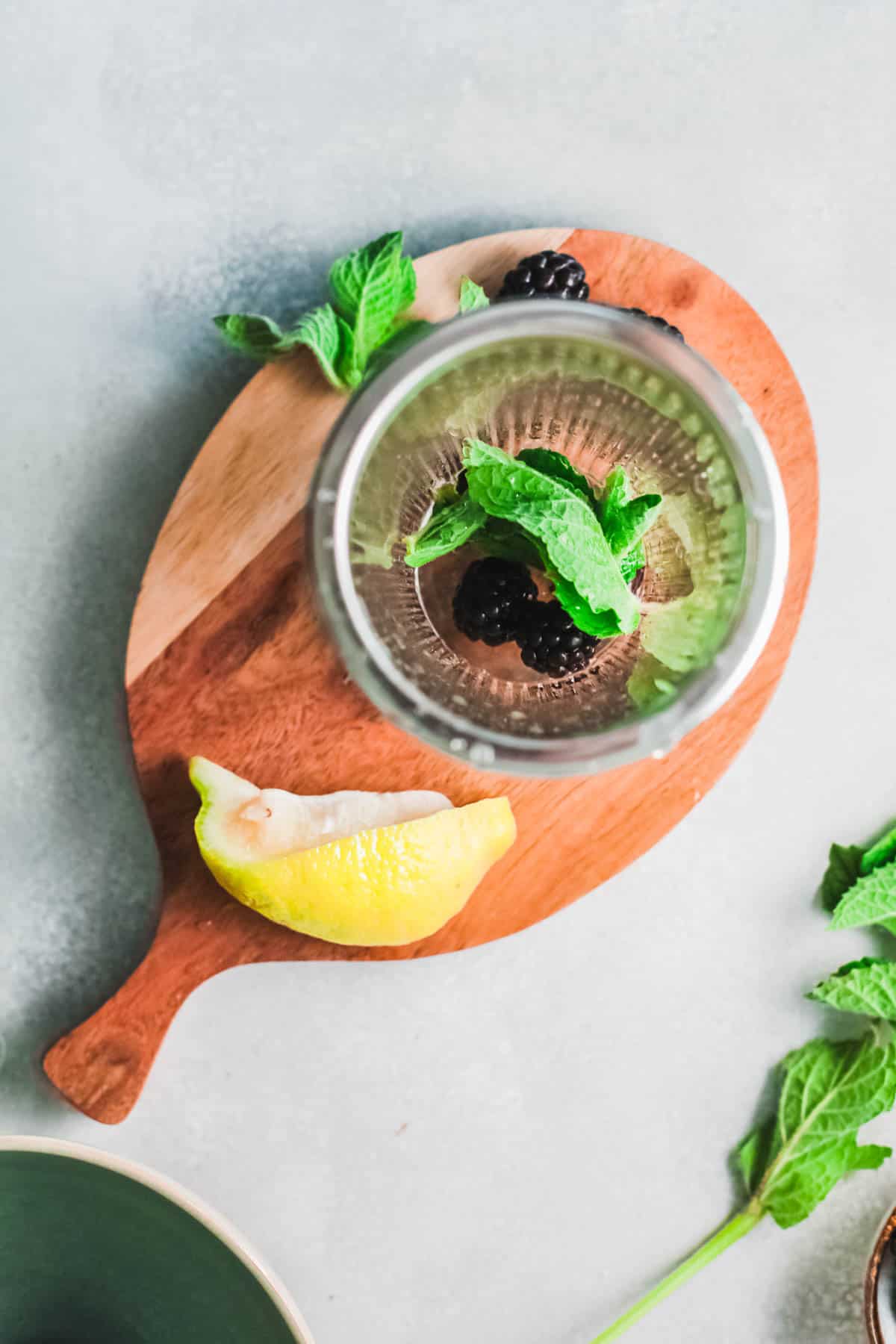 Overhead view of a cutting board holding a lemon, blackberries and fresh mint to make a cocktail.