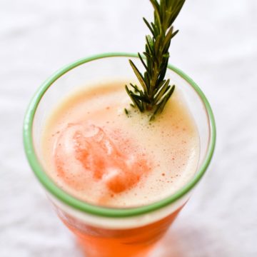 Overhead shot of a cocktail glass with a blood orange sorbet in a gin cocktail with a rosemary sprig.