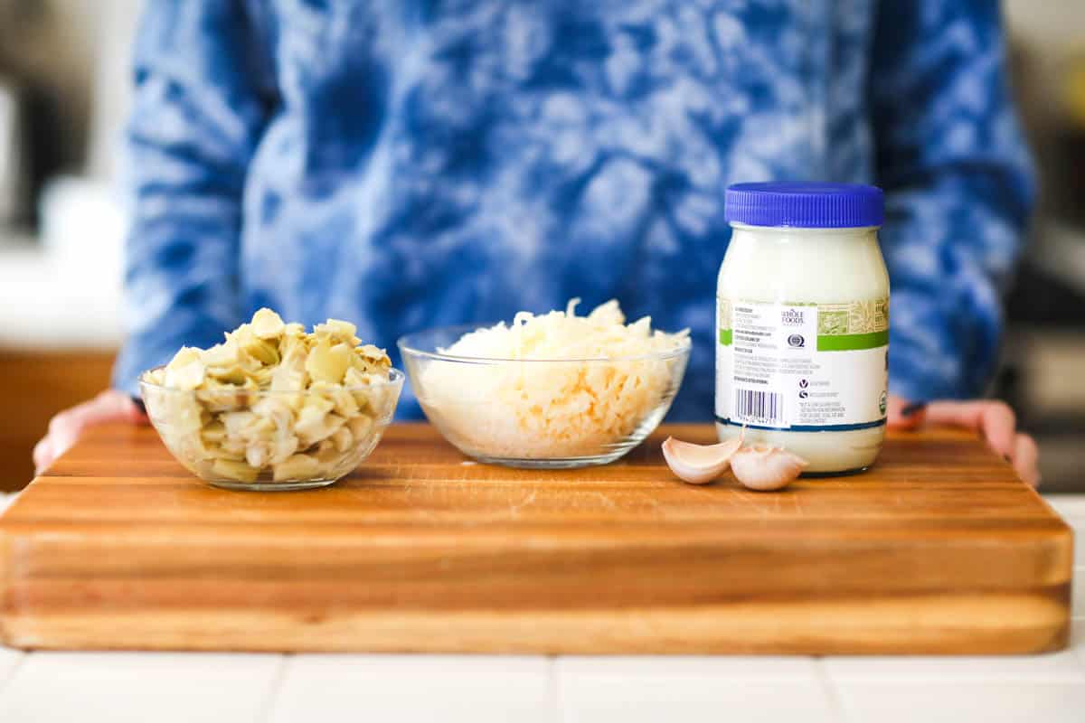 Ingredients for Artichoke Dip on a wooden cutting board.